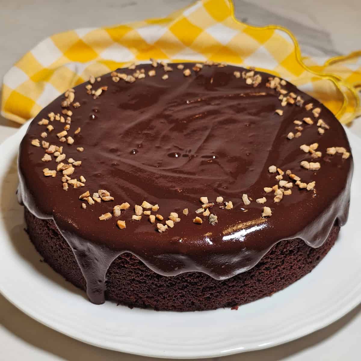 Vegan gluten-free Nutella cake with glossy chocolate topping and chopped hazelnuts