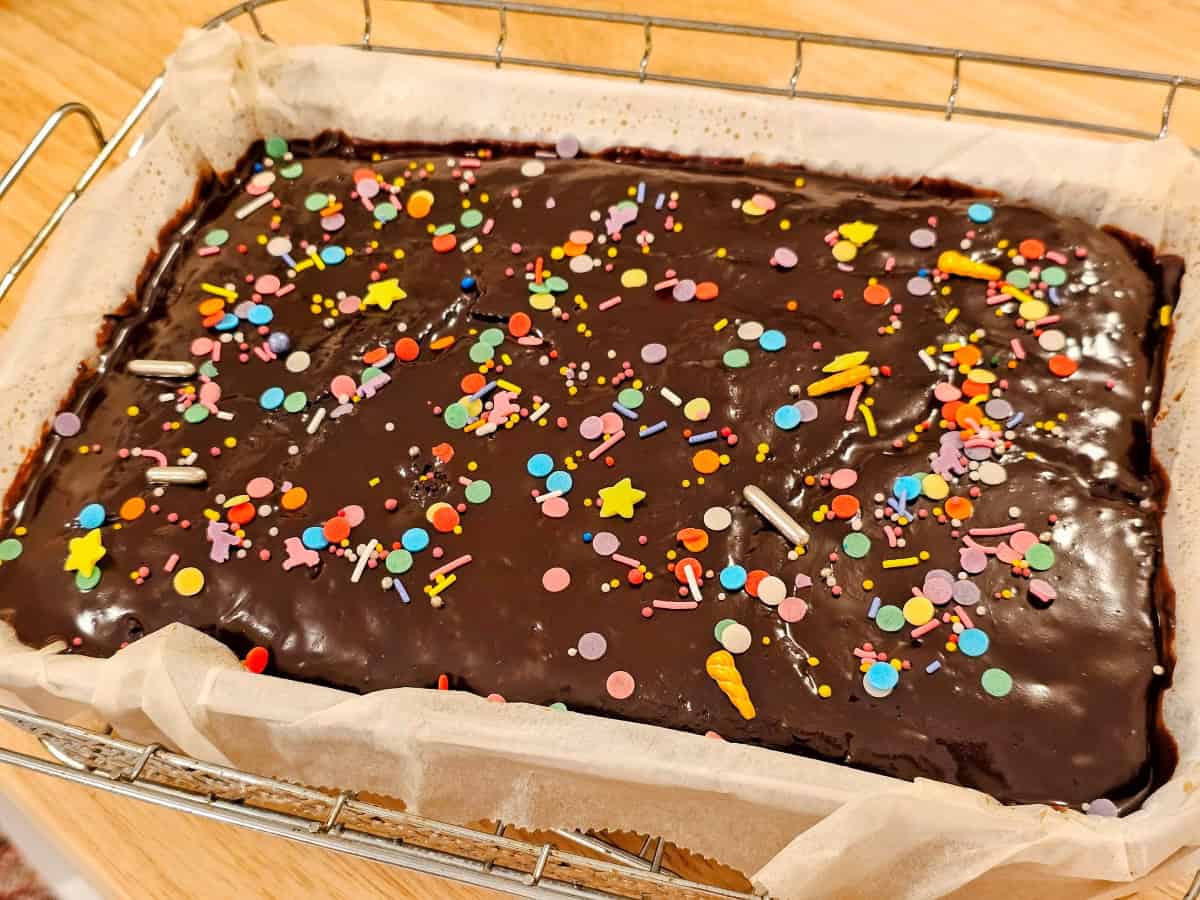 Vegan chocolate cake topped with shiny glaze and colorful sprinkles, photographed from above
